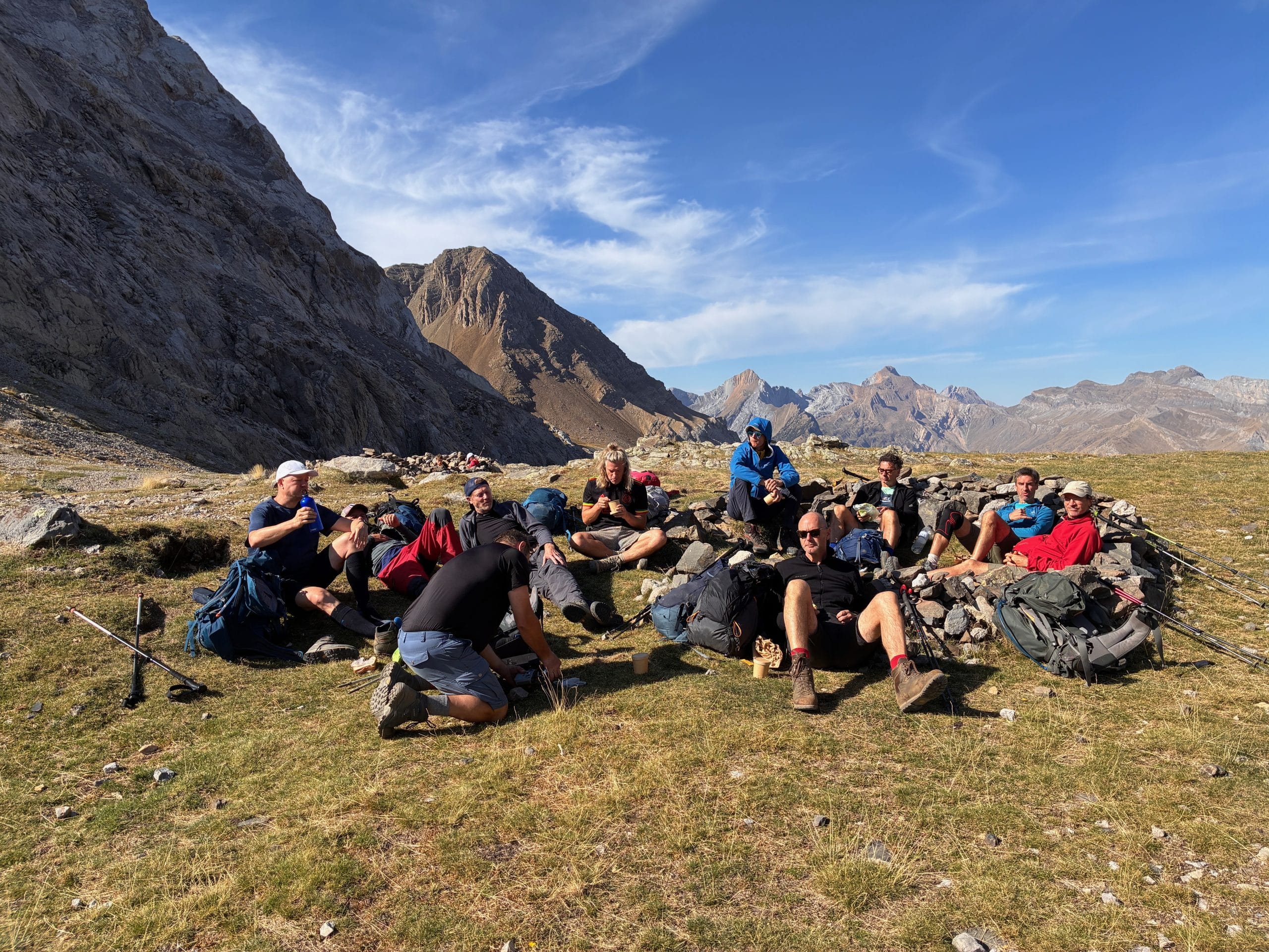 Vriendengroep geniet van een gezamenlijke pauze tussen de hoge bergen tijdens een meerdaagse wandeltocht in de Pyreneeën